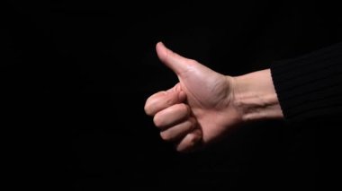 Kadın elinin baş parmağı, karanlığa yakın bir hareket gibi, siyah arka plana karşı.
