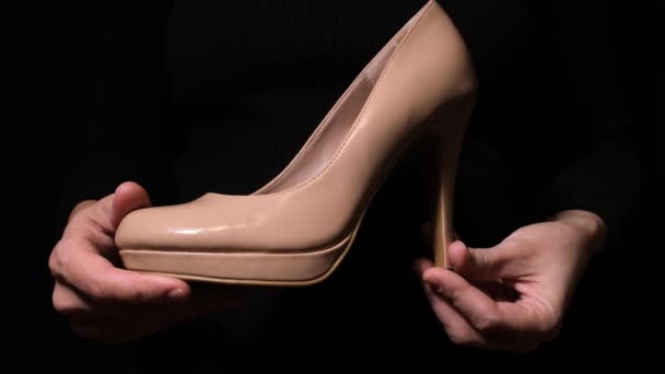 Manos que sostienen elegante zapato de tacón alto de charol beige sobre fondo negro — Vídeo de stock