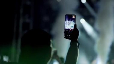 Müzik festivalinde ellerinde telefon olan izleyiciler. Bir müzik festivalinde çok renkli ışık. Konserde dans hayranları. En sevdikleri grubun konserinde mutlu kalabalık.