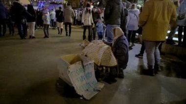 Kyiv, Ukrayna, 7 Ocak. 2022: Şehir meydanındaki evsiz kadın köpek maması için para istiyor. Hayırsever merhamet gönüllü barınağa yardım eder. Sokakta karton kutularda aç köpekler..