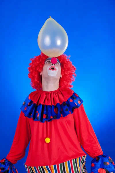 Palhaço feliz com balão no fundo azul — Fotografia de Stock