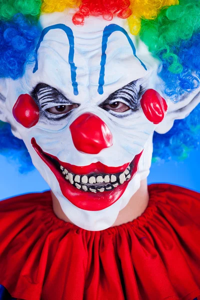 Strašidelný klaun člověk v masce klauna na modrém pozadí — Stock fotografie