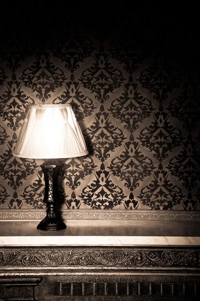 Vintage lamp on old fireplace in room with red rocco pattern