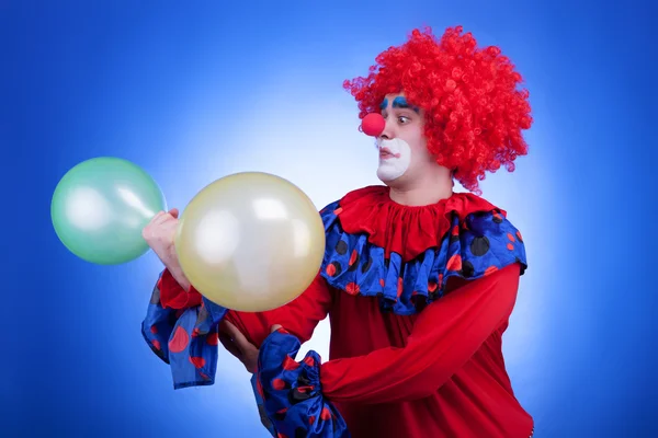 Clown avec deux ballons à la main sur fond bleu — Photo