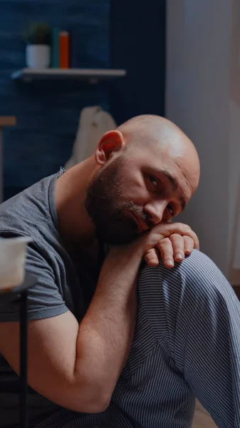 Депрессивный мужчина сидит на полу и смотрит в камеру с разочарованным выражением лица — стоковое фото