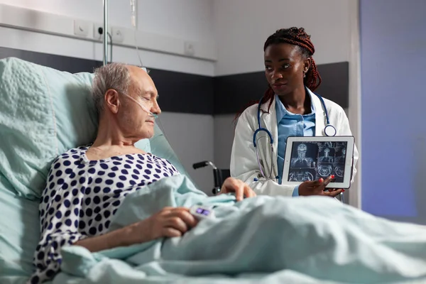 Afro-Amerikaanse arts zit naast senior man uit te leggen lichaam trauma — Stockfoto