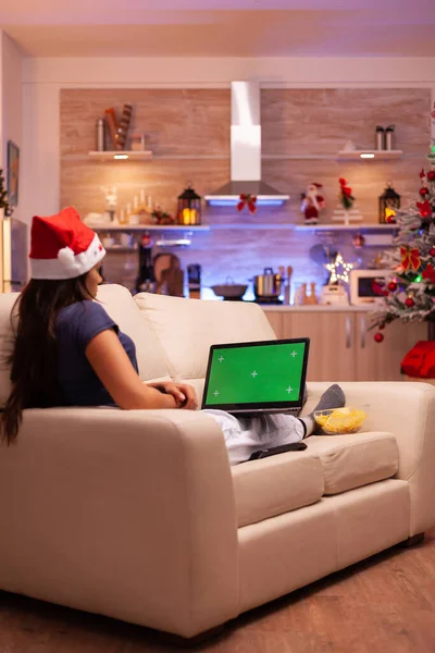 Žena osoba odpočívající na pohovce ve vánočním zdobené kuchyni drží zelenou obrazovku napodobit chroma klíč lapto — Stock fotografie