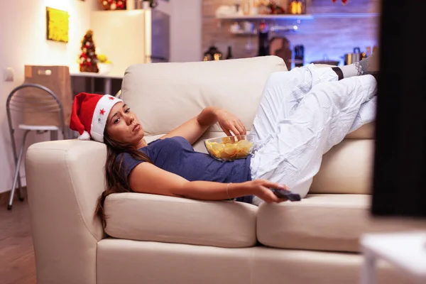 Woman relaxing on couch eating snacks while watching xmas comedy movie on tv — Stock Photo, Image