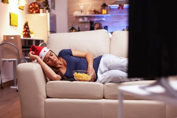 Mujer cansada durmiendo en el sofá mientras ve películas de Navidad en la televisión — Foto de Stock