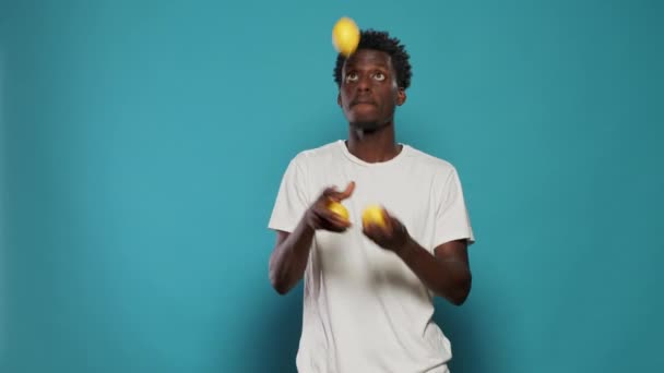 Juguetón adulto malabarismo limones y de pie sobre fondo azul — Vídeo de stock