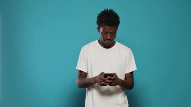 Afrikalı Amerikalı adam heyecanlanıyor ve akıllı telefon kullanıyor. — Stok video