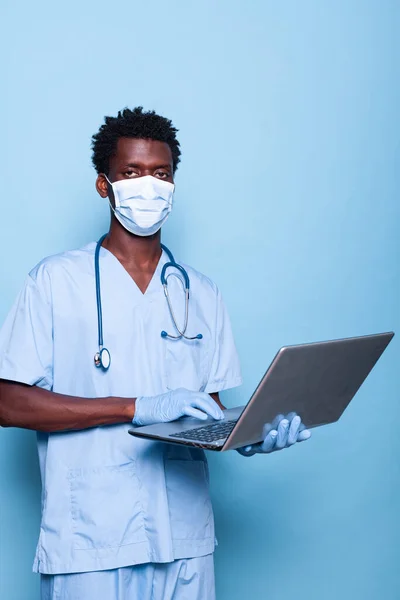 Black nurse holding laptop while looking at camera in studio — Stock Photo, Image