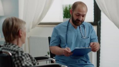 Engelli kıdemli hasta, hemşireyle tedavi hakkında konuşuyor.