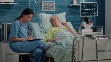 Yatakta hastalıklı kıdemli bir hastayla konuşan tıbbi asistan.