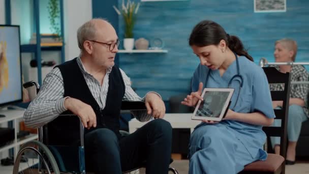 Enfermera mostrando osteopatía rayos X en la tableta a un anciano inválido — Vídeos de Stock