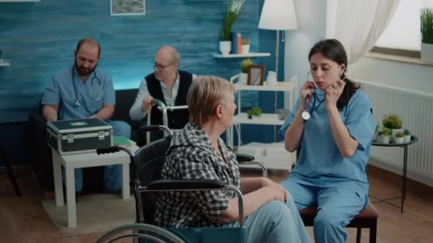 Пенсионерка в инвалидном кресле получает консультацию от медсестры — стоковое видео
