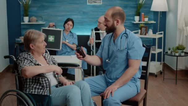 Pielęgniarka mężczyzna daje butelkę tabletek staremu pacjentowi niepełnosprawnemu — Wideo stockowe
