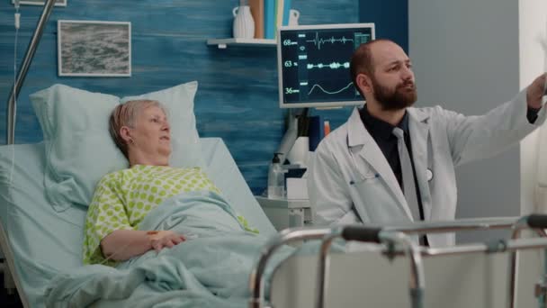 Doctor and elder woman in bed looking at x ray scan — Stock Video