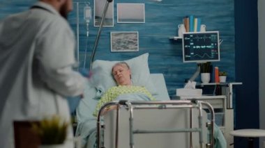 Doktor ve hemşire yaşlı hastaya yatakta yardım ediyor.