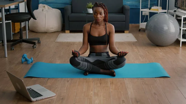 Flessibile sottile donna nera seduta in posizione loto sulla mappa yoga in soggiorno — Foto Stock