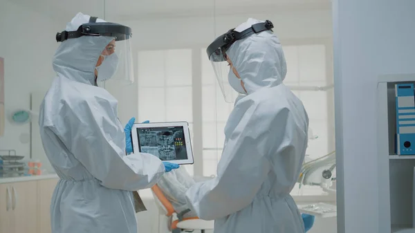 Equipo de dentistas vistiendo trajes de ppe mientras miran rayos X — Foto de Stock