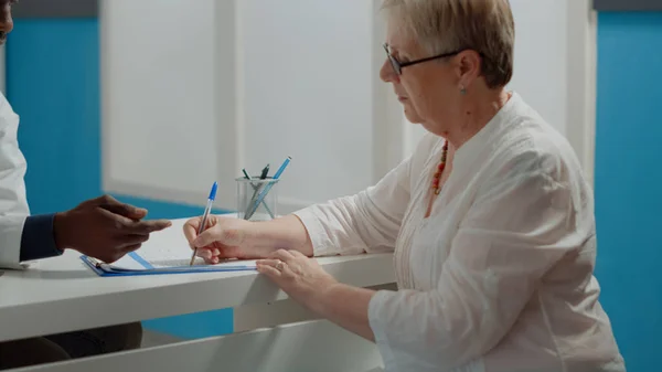 Close up of elder patient signing checkup documents — Stock Photo, Image