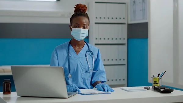Ritratto di infermiera seduta alla scrivania con computer portatile e documenti — Foto Stock