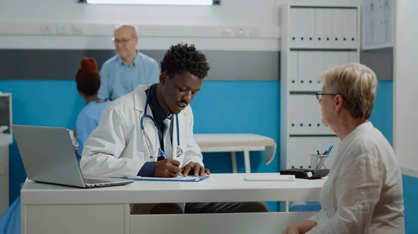 非裔美国医生在笔记本上写检查 — 图库照片