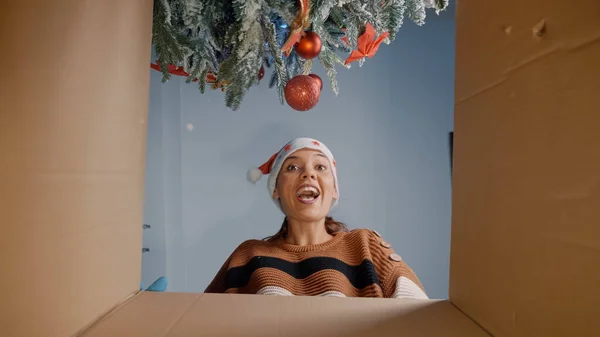 Young woman opening christmas present under tree