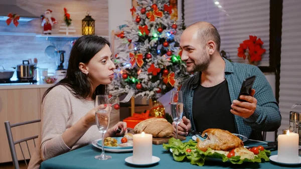 Kadın ve erkek akıllı telefona bakarak şenlikli bir akşam yemeği yiyorlar. — Stok fotoğraf