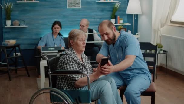 Asistent medical care predă o bătrână cu handicap să folosească smartphone-ul — Videoclip de stoc