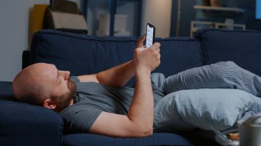 Ayrılmanın neden olduğu üzgün bir adam. Evdeki kanepede uzanmış akıllı telefonlara bakıyor.