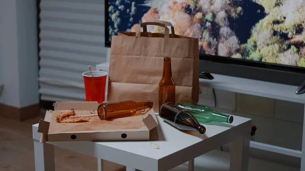 Mesa desordenada con botellas de cerveza vacías y restos de comida en la sala de estar —  Fotos de Stock