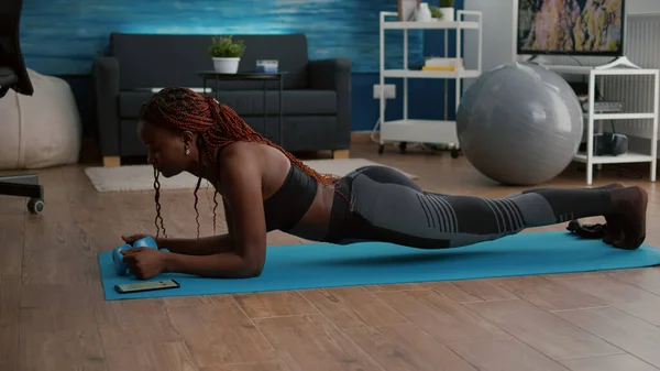 Flessibile sottile donna nera che allunga i muscoli del corpo mettendo cronometro sul telefono — Foto Stock