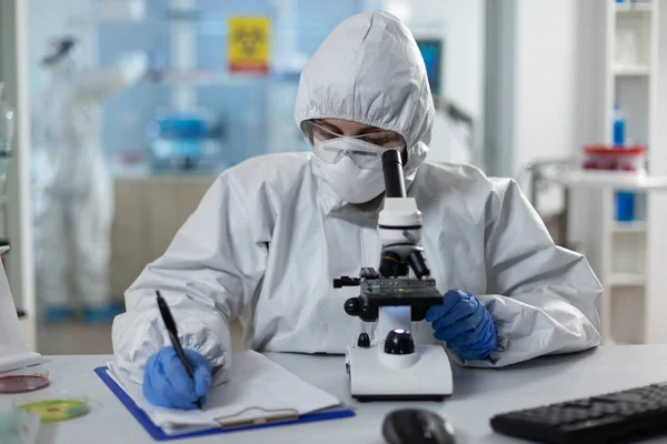 生物学家穿着防护服，用医用显微镜分析化学物质 — 图库照片