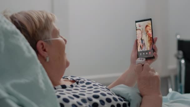 Pacjent w podeszłym wieku rozmawiający przez telefon wideo z siostrzenicą i córką — Wideo stockowe