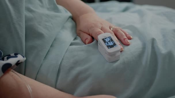 Κοντινό πλάνο του χεριού του ηλικιωμένου ασθενούς με οξύμετρο στο κρεβάτι — Αρχείο Βίντεο