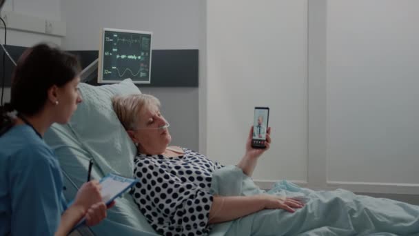 Пожилой пациент держит смартфон для видеозвонка с врачом — стоковое видео
