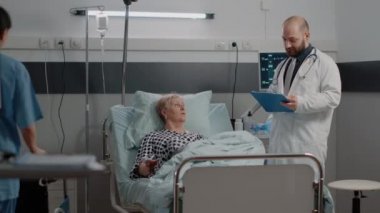 Doktor ve hemşire hasta hastanın yataktan kalkmasına yardım ediyor.