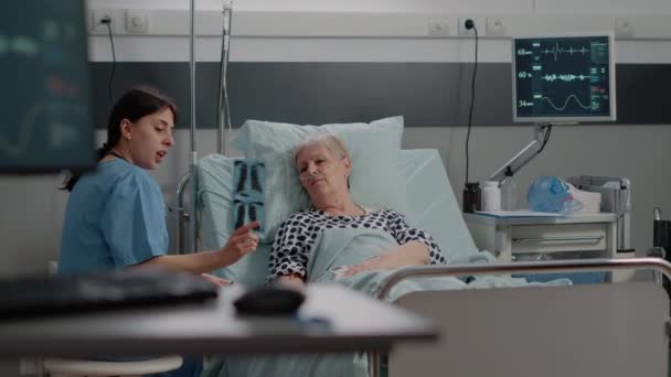 Arzthelferin zeigt auf Röntgenbild für kranke Seniorin — Stockvideo