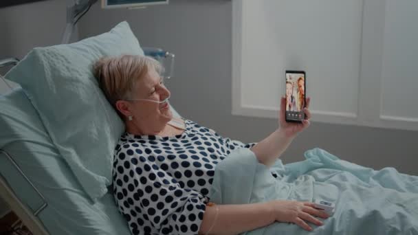 Старший пацієнт розмовляє з родиною на відеодзвінок у лікарняному ліжку — стокове відео