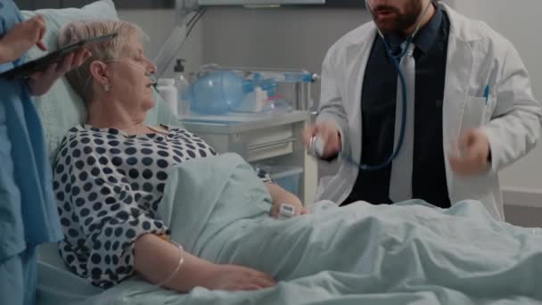 Zespół medyczny robi wizytę kontrolną dla starszego pacjenta w łóżku — Wideo stockowe