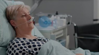Yatakta yatan genzinde oksijen tüpü olan yaşlı kadın portresi.