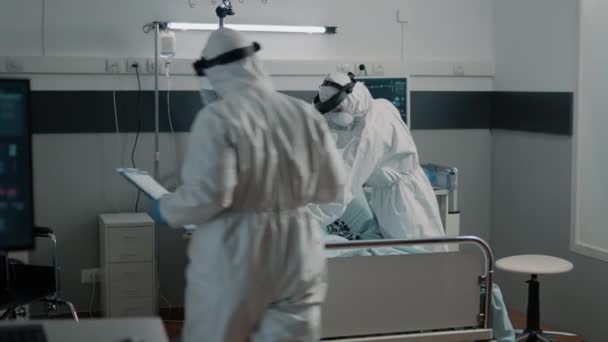 Команда парамедиков в защитных костюмах проверяет состояние здоровья пациентов — стоковое видео