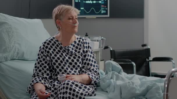 Mulher doente com tubo de oxigênio nasal e saco de gotejamento IV sentado na cama — Vídeo de Stock