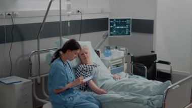 Hemşire yatağında hastalık olan yaşlı bir hastaya yardım ediyor.