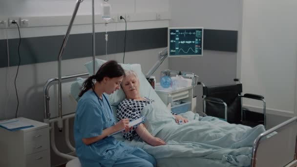 Nurse giving assistance to senior patient with disease in bed — Stock Video