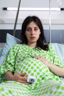 Hastane koğuşunda oturan yorgun ve hamile birinin portresi.