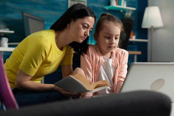 Mother helping daughter with school homework reading literature book