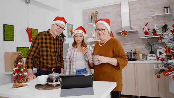 Šťastná rodina nosí Santa klobouk, zatímco stojí v kuchyni zdobené vánoční pozdrav vzdálených přátel — Stock fotografie